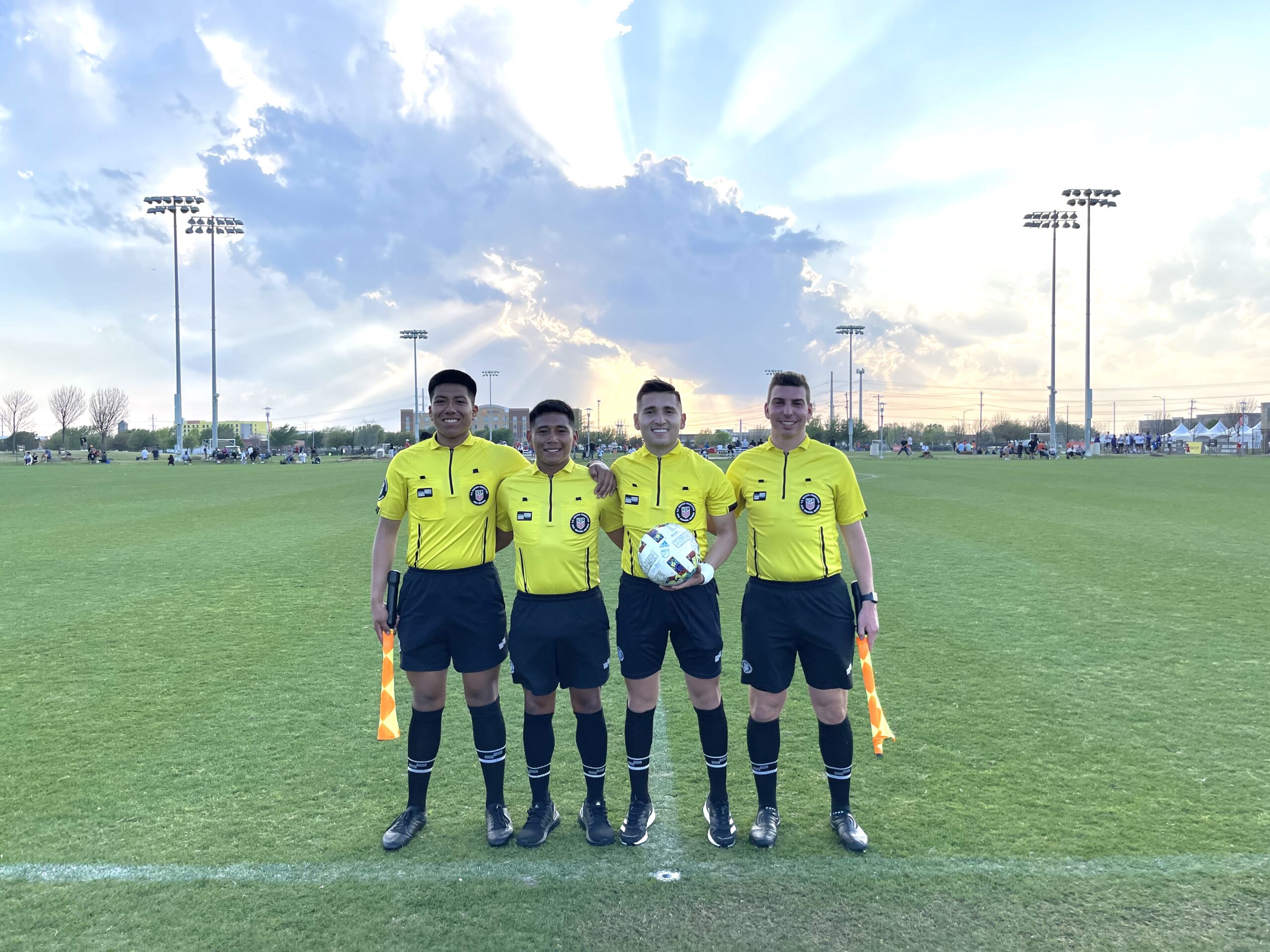 Four referees in yellow holding flags and ball smiling